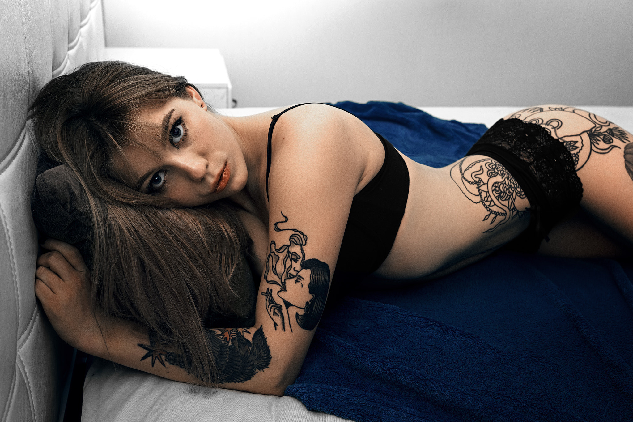 Девушка с татуировкой раздевается на постели 