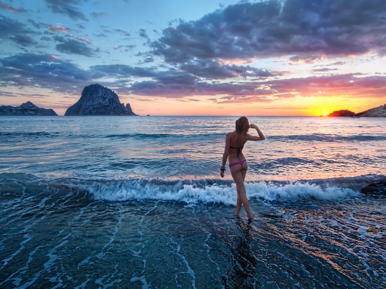 Обнаженная девушка на каменистом пляже у моря